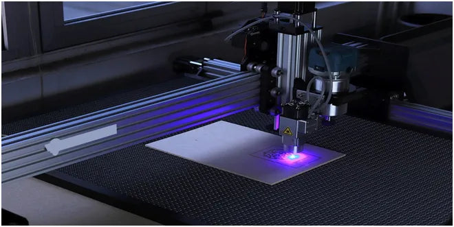Laser engraving machine in operation with a purple light on a dark surface.
