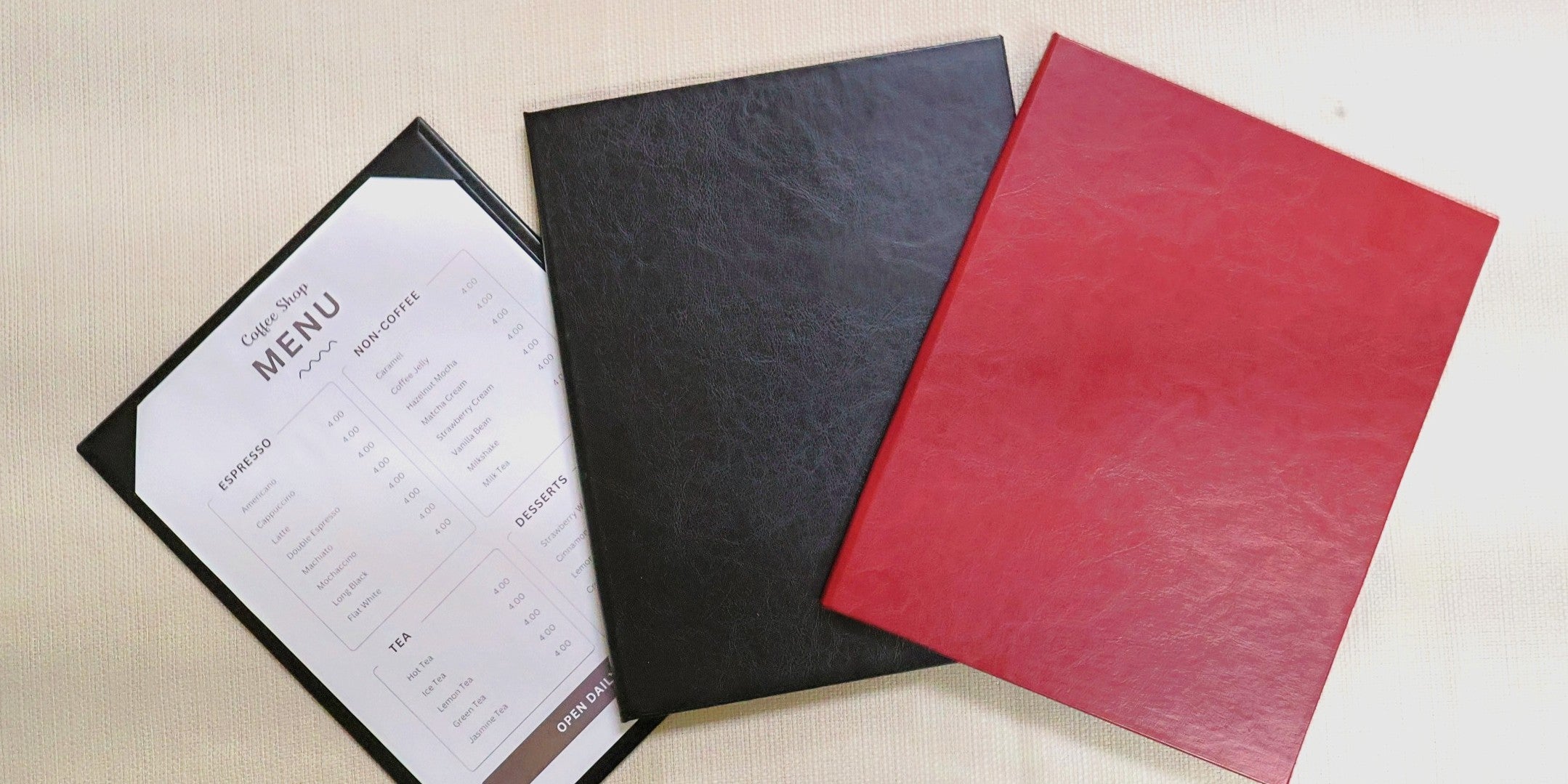 Three menu covers in black, red, and white on a beige surface