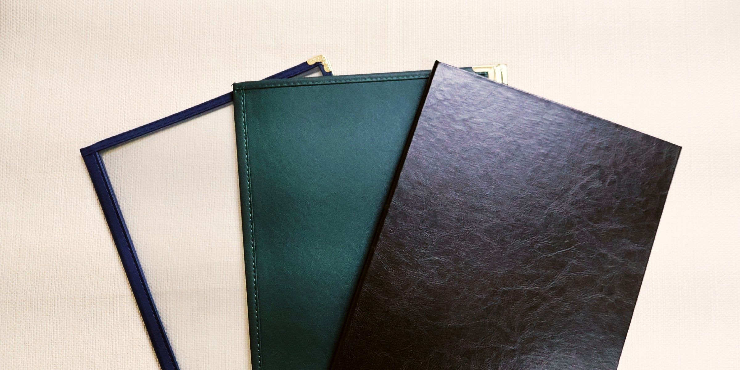 Three leatherette menu covers in different colors on a light background